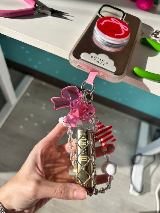 Silver metallic mesh Lippie Clippie keychain attached to a phone case, designed to securely hold and carry standard-sized lipsticks as a functional and stylish mobile accessory.