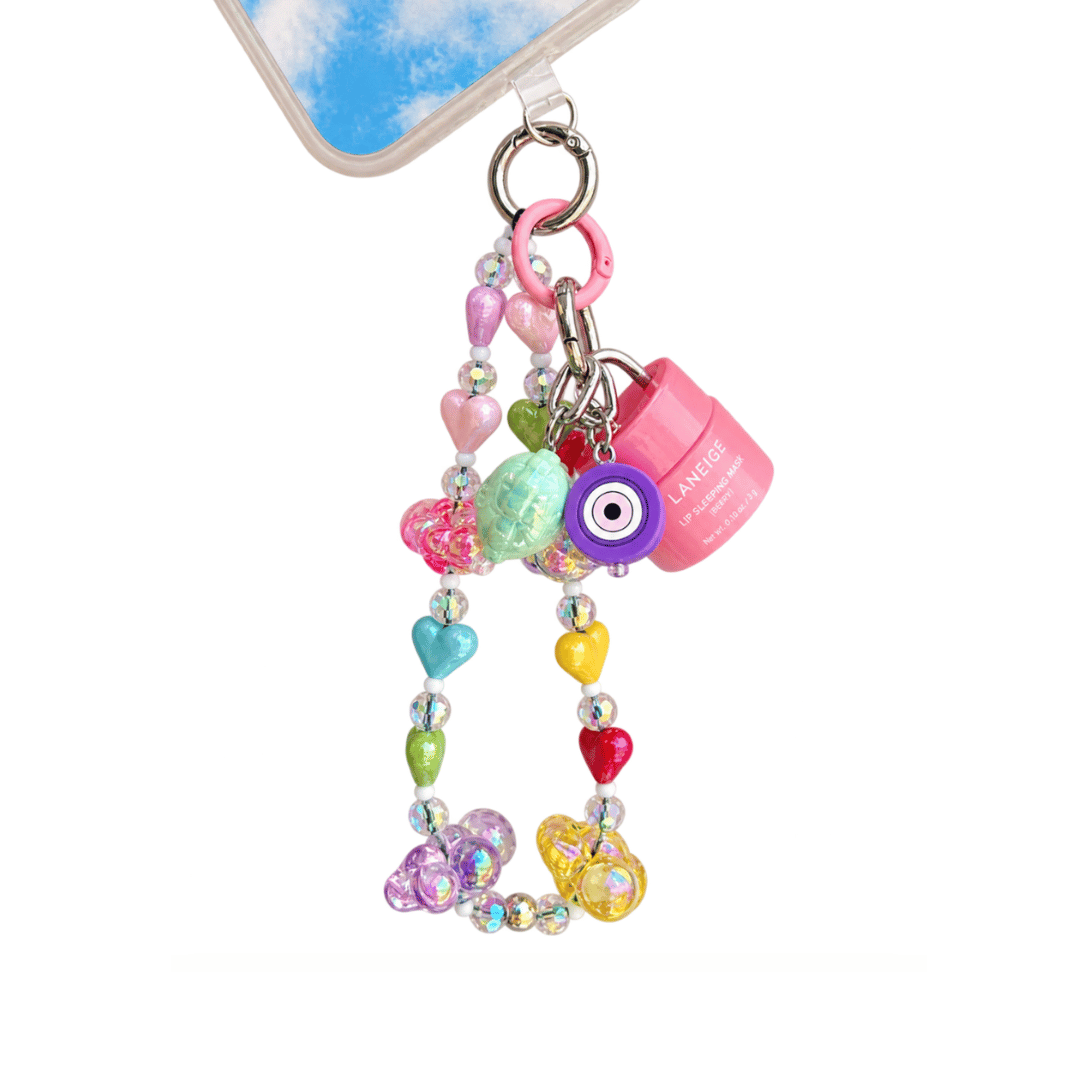 A colorful phone strap charm featuring a pink padlock, heart-shaped beads, a purple evil eye charm, and a butterfly charm, shown attached to a clear phone case on a white background.