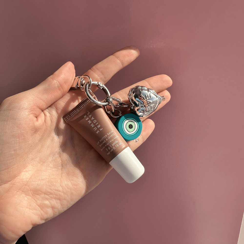 Heart charm shown with a teal evil eye charm clipped to a lip balm tube, Build A Caze.