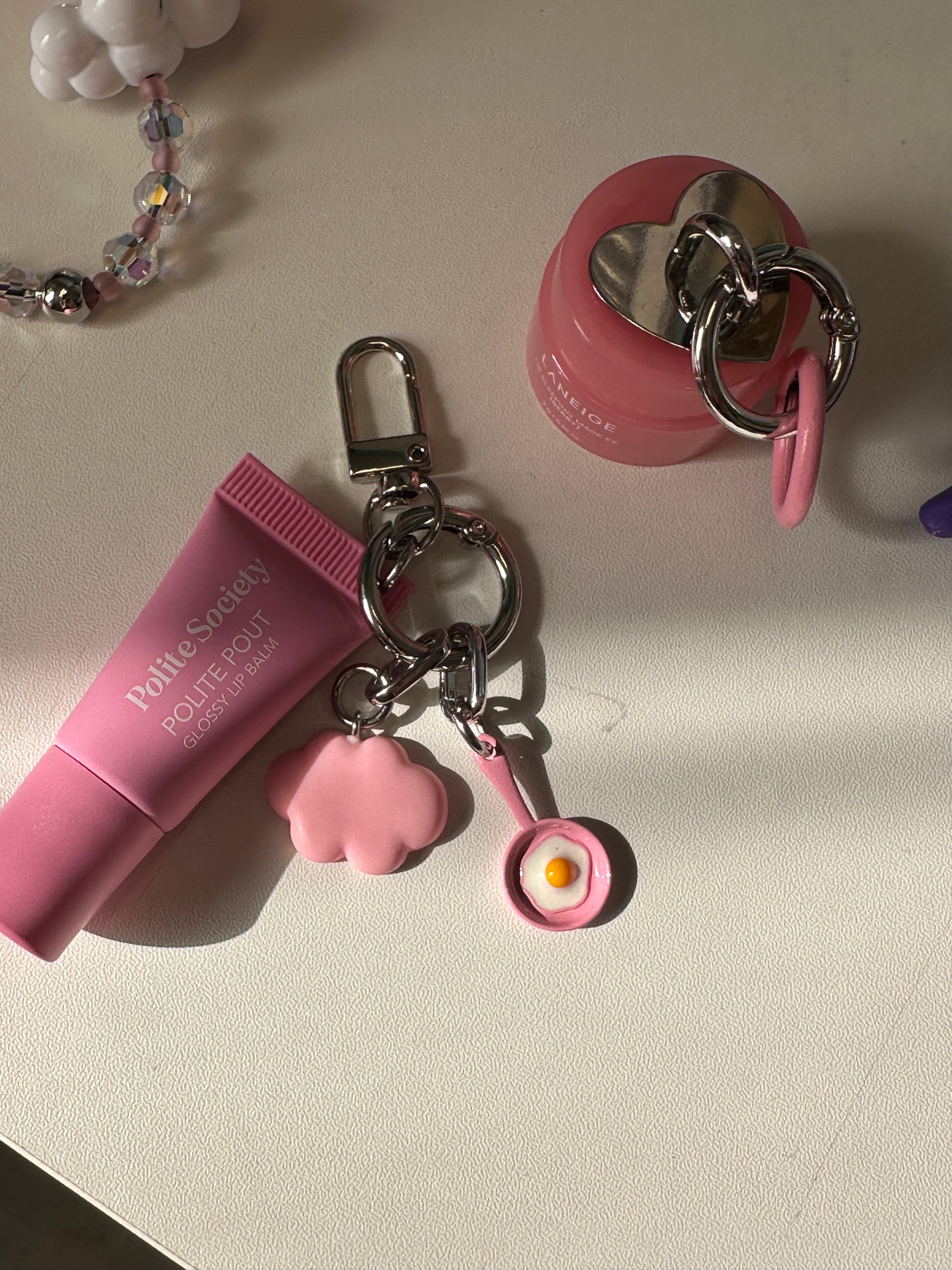 Pink Sunny Side Up Charmie clipped to a lip gloss tube on a table, next to a beaded  lip gloss Build A Caze