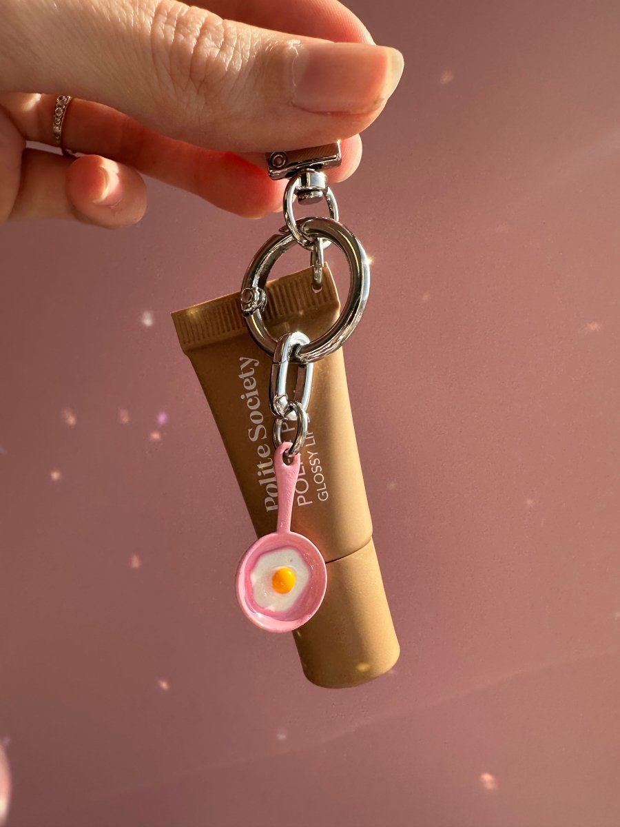 Hand holding a lip gloss tube with the Pink Sunny Side Up Charmie clipped onto the keyring	